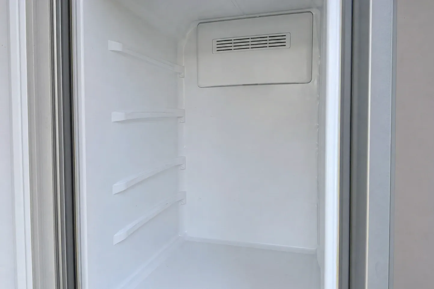 Empty white column interior with shelf rails down one wall, a louvred vent high on the back wall and the door seal along each edge
