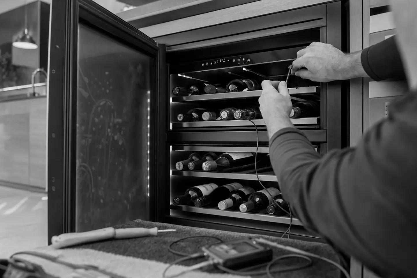 Black-and-white frame of an undercounter wine cabinet with the glass door open and a probe held at the top shelf