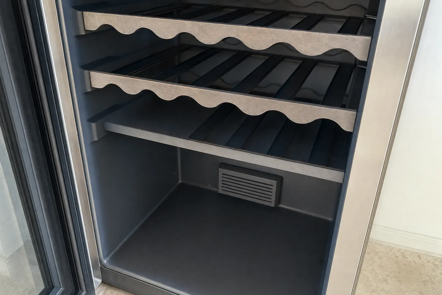 Empty wine cabinet with scalloped wooden shelf fronts and a louvred rear vent, the open glass door showing its seal channel